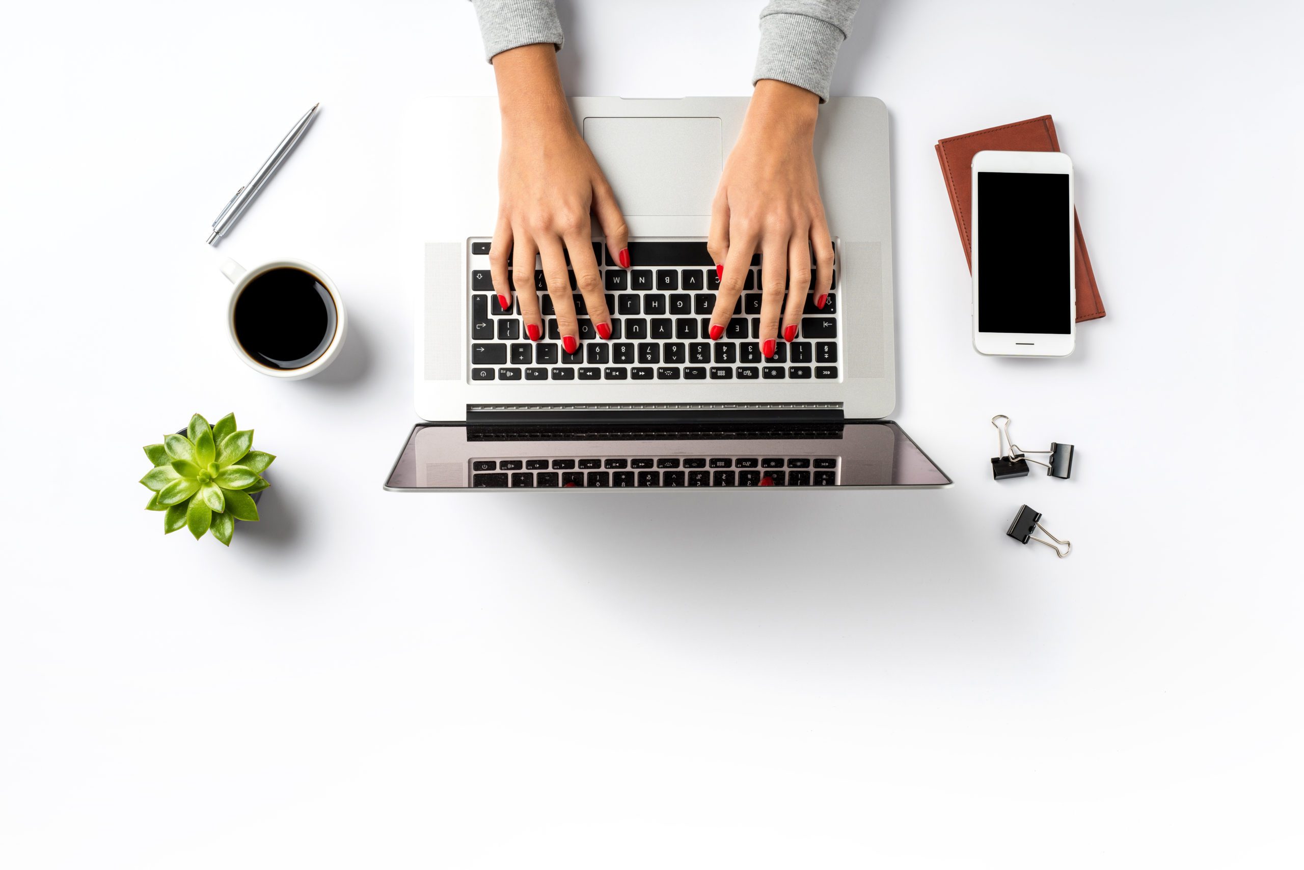 woman typing on laptop with phone and coffee
